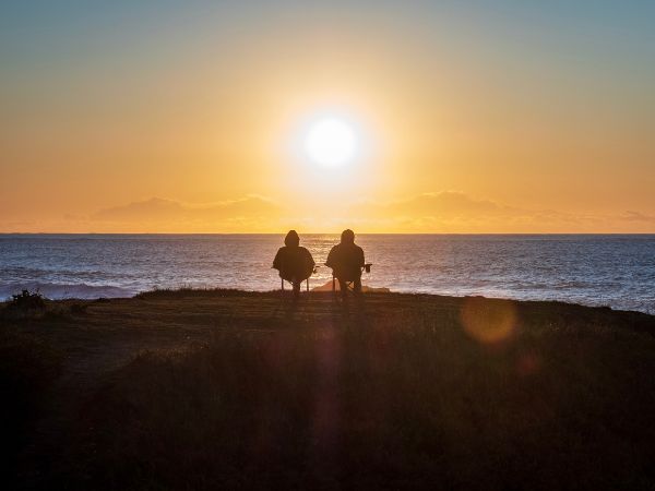 Rentensystem der USA und der 401k: Zwei Personen blicken auf den Sonnenuntergang über dem Meer