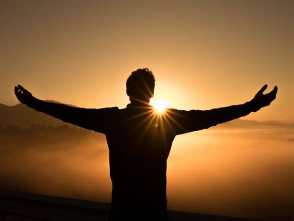 Ein Mensch steht mit offenen Armen vor der untergehenden Sonne