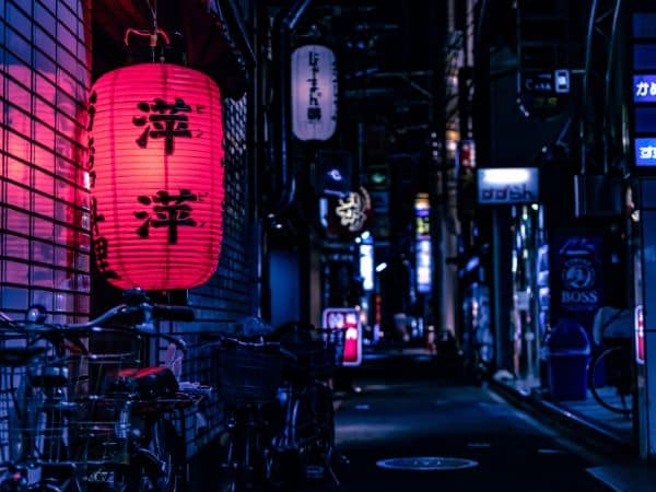 Eine Gasse in einer japanischen Großstadt bei Nacht. Eine rote Laterne leuchtet.